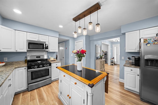 kitchen featuring a kitchen island, pendant lighting, light wood-style floors, stainless steel appliances, and white cabinetry