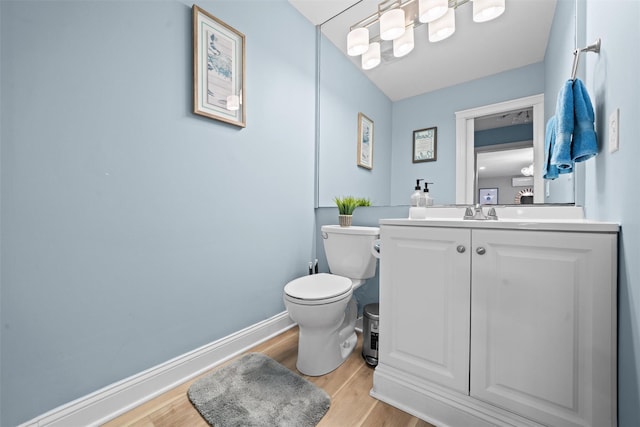 half bath featuring baseboards, wood finished floors, toilet, and vanity