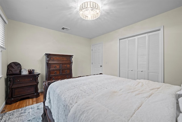 bedroom featuring visible vents, wood finished floors, baseboards, a closet, and a notable chandelier