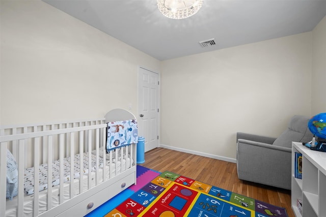 bedroom featuring visible vents, a crib, baseboards, and wood finished floors