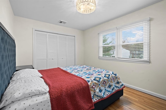 bedroom with baseboards, visible vents, wood finished floors, and a closet