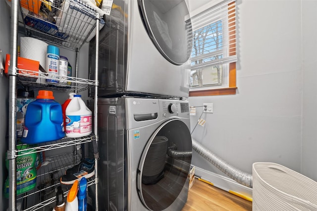clothes washing area featuring baseboards, stacked washer / drying machine, wood finished floors, and laundry area