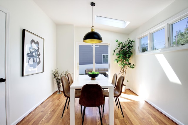 dining space with baseboards, a skylight, and light wood-style floors