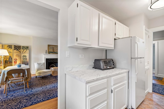 kitchen featuring freestanding refrigerator, a toaster, white cabinets, light stone counters, and a premium fireplace