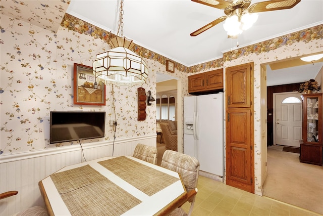 dining space with a wainscoted wall, ornamental molding, a ceiling fan, and wallpapered walls