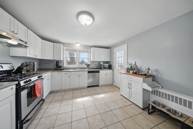 kitchen featuring radiator heating unit, under cabinet range hood, a sink, light tile patterned floors, and stainless steel appliances
