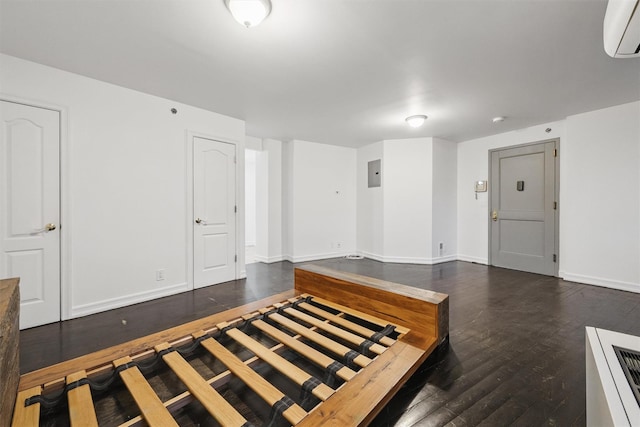 unfurnished bedroom with electric panel, baseboards, a wall mounted AC, and dark wood-type flooring