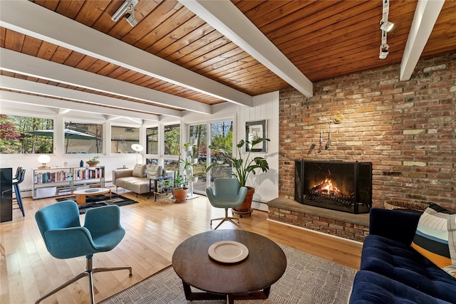 living room with baseboard heating, a brick fireplace, rail lighting, hardwood / wood-style floors, and beamed ceiling