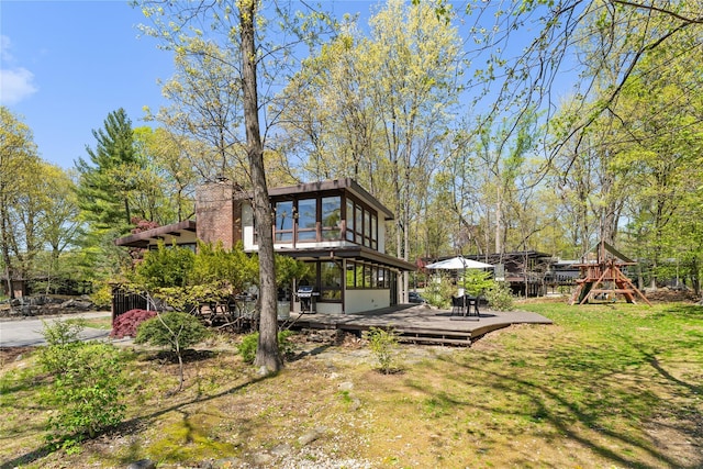 view of yard featuring a playground, a wooden deck, and a sunroom