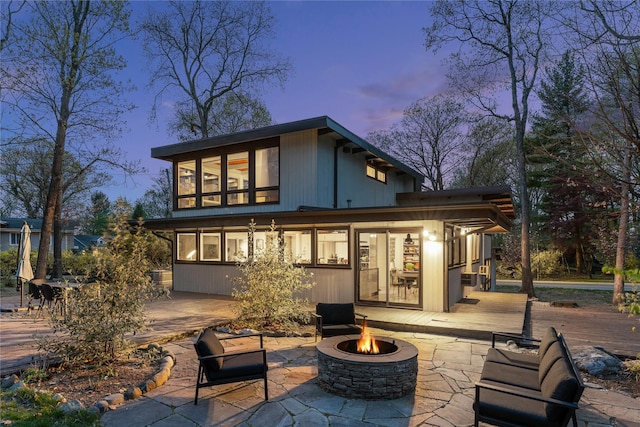 back of property at dusk with a wooden deck, a fire pit, and a patio area