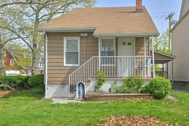 view of front of home featuring a shingled roof, a front yard, and a chimney