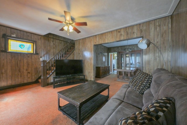 living room with carpet floors, ceiling fan, wood walls, and stairway