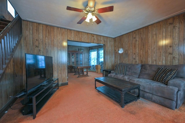 living room with stairway, ceiling fan, wood walls, and carpet