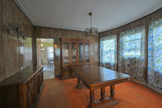 carpeted dining room featuring wood walls and a chandelier