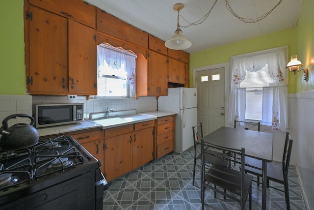 kitchen with backsplash, gas stove, stainless steel microwave, freestanding refrigerator, and tile counters