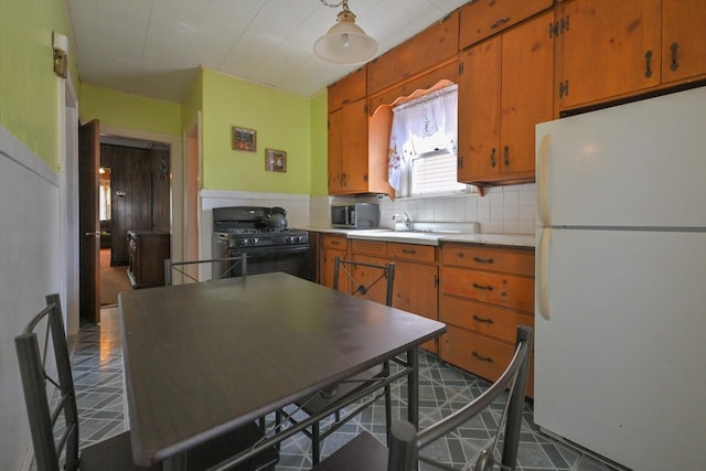 kitchen with freestanding refrigerator, brown cabinets, stainless steel microwave, and gas stove