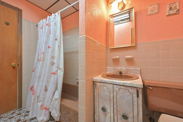 full bathroom with a textured wall, vanity, toilet, shower / bath combo with shower curtain, and tile walls