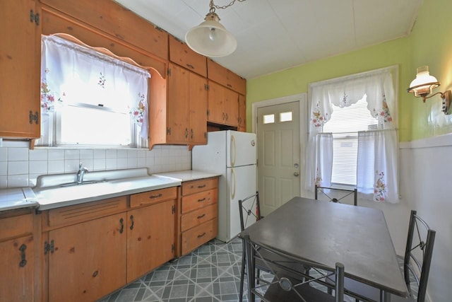 kitchen with light countertops, freestanding refrigerator, a sink, and tasteful backsplash