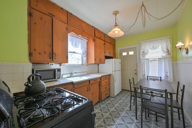 kitchen featuring decorative backsplash, brown cabinetry, black gas stove, a sink, and stainless steel microwave