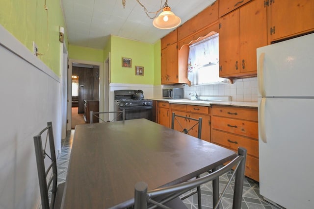 kitchen with black gas stove, freestanding refrigerator, stainless steel microwave, and brown cabinetry