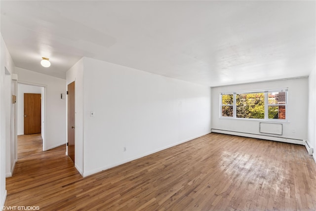 spare room featuring baseboards, a baseboard heating unit, and wood finished floors