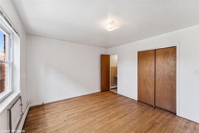 unfurnished bedroom featuring a baseboard radiator, a closet, wood finished floors, and multiple windows