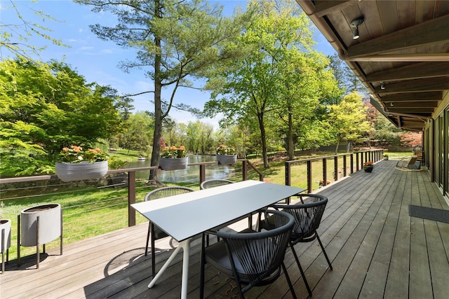 wooden terrace featuring a lawn, a water view, and outdoor dining space