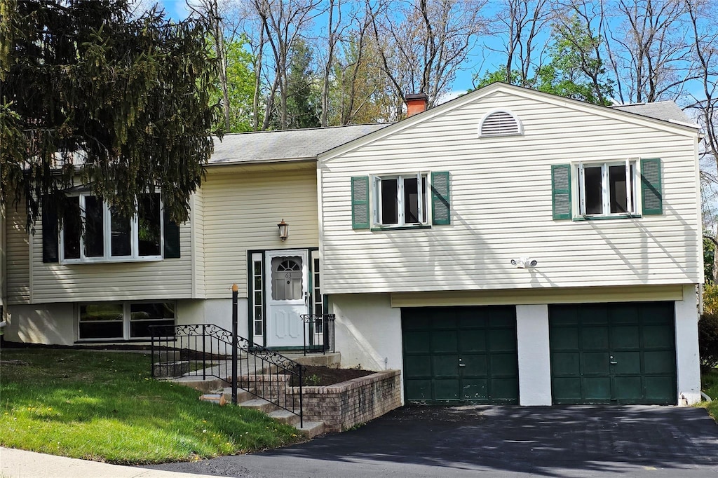 bi-level home with an attached garage, a front yard, driveway, and a chimney
