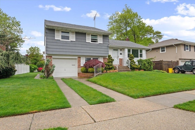 tri-level home featuring a garage, fence, a front yard, brick siding, and driveway