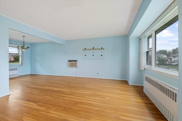 unfurnished living room featuring a notable chandelier, light wood finished floors, baseboards, and radiator heating unit