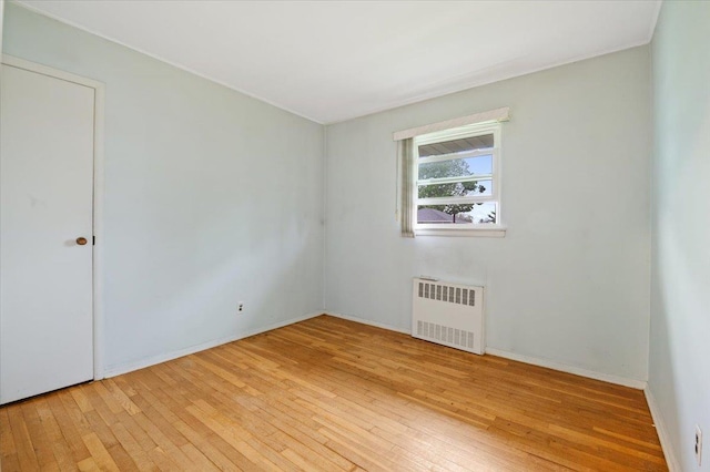 unfurnished room featuring baseboards, radiator heating unit, and hardwood / wood-style flooring