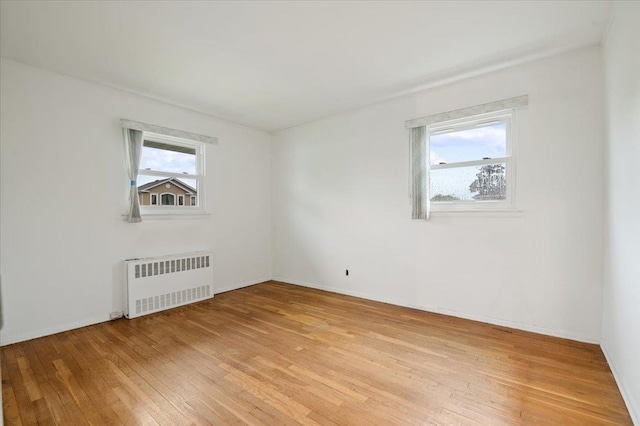 unfurnished room featuring baseboards, light wood-type flooring, and radiator heating unit