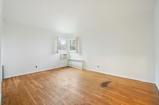 empty room with light wood-style floors, a wall mounted AC, baseboards, and radiator heating unit