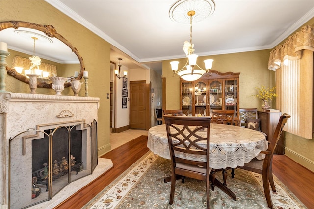 dining space featuring crown molding, a chandelier, baseboards, a fireplace, and wood finished floors