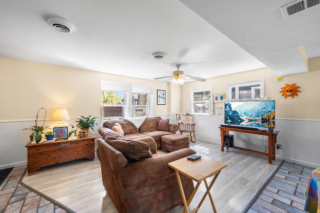 living area featuring visible vents, wainscoting, ceiling fan, and light wood finished floors