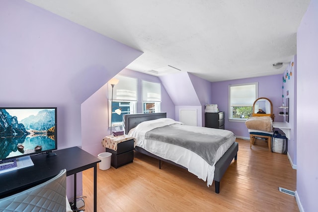 bedroom with baseboards, visible vents, vaulted ceiling, and light wood finished floors