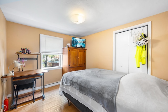 bedroom featuring a closet, baseboards, a baseboard heating unit, and wood finished floors
