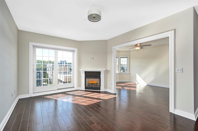 unfurnished living room featuring baseboards, a ceiling fan, a glass covered fireplace, and wood finished floors