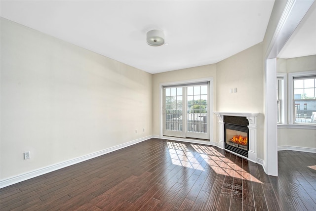 unfurnished living room featuring dark wood-style flooring, baseboards, a glass covered fireplace, and a healthy amount of sunlight