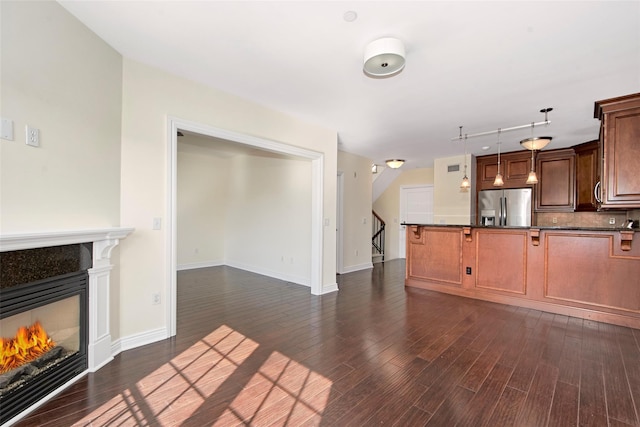 unfurnished living room with dark wood-type flooring, baseboards, and a glass covered fireplace