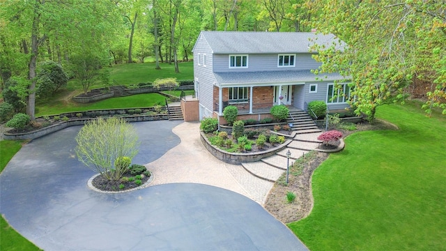 view of front facade featuring covered porch, roof with shingles, stairs, a front lawn, and curved driveway
