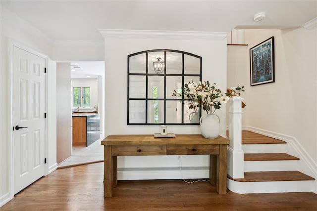 entryway with a baseboard heating unit, wood finished floors, crown molding, and stairs