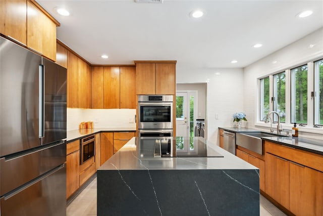kitchen featuring modern cabinets, a sink, washing machine and clothes dryer, backsplash, and appliances with stainless steel finishes