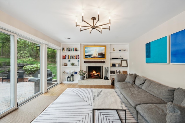 living room with a large fireplace, built in features, wood finished floors, and a notable chandelier