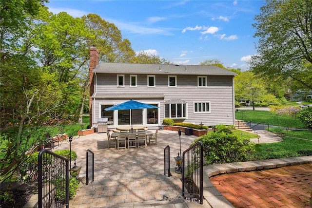 back of house with a gate, outdoor dining space, a chimney, fence, and a patio area