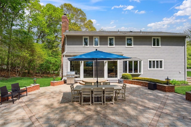 rear view of property featuring a yard, a patio area, outdoor dining space, and a chimney