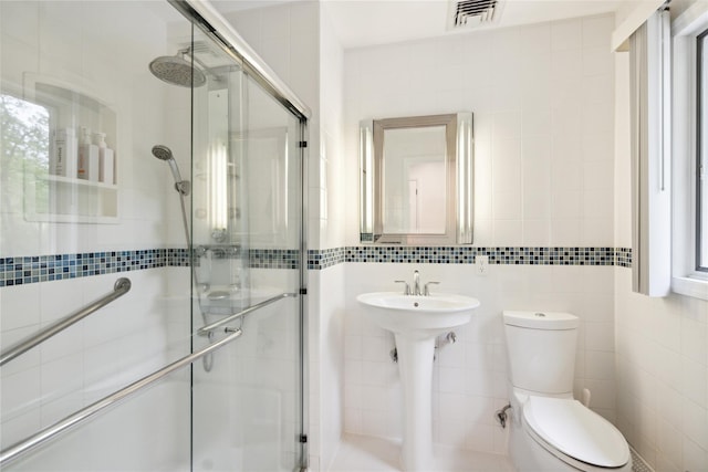bathroom featuring toilet, a stall shower, a sink, tile walls, and visible vents