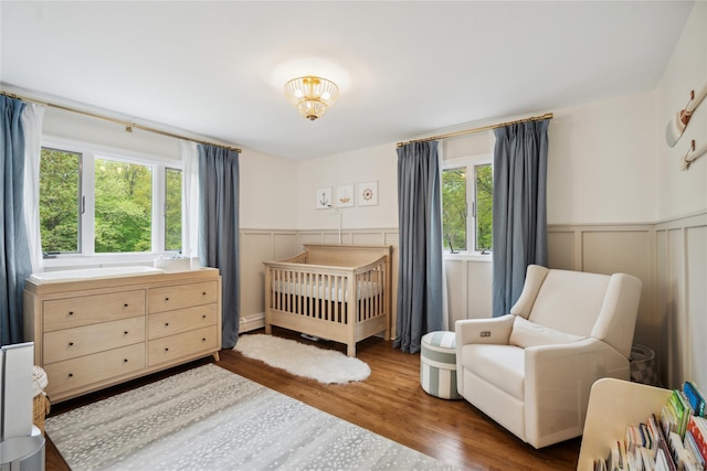 bedroom with a crib, a decorative wall, a wainscoted wall, and wood finished floors