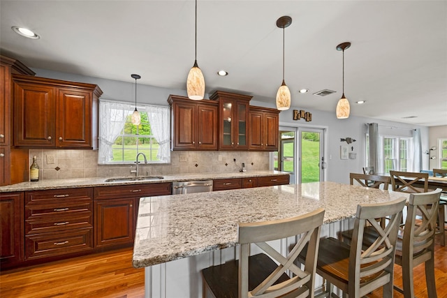 kitchen featuring a sink, dishwasher, light wood-type flooring, visible vents, and a kitchen bar
