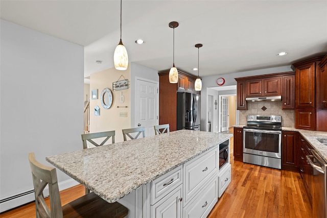 kitchen with under cabinet range hood, stainless steel appliances, a breakfast bar, and light wood-style floors